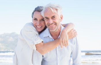 Happy senior couple with perfect smiles enjoying a sunny day on a beach.