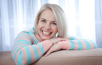 Happy mature woman with a perfect smile leaning over a sofa.