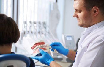 A dentist with a dental model explaining restorative treatment options to a patient sitting in a dental chair.