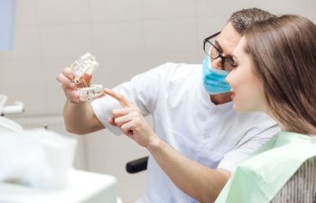 A dentist with a dental model explaining restorative treatment options to a woman patient.